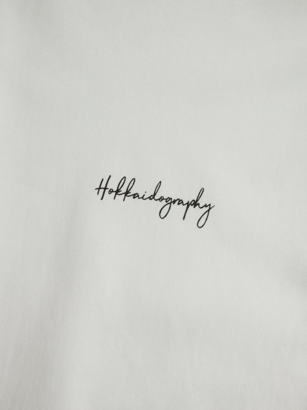 左胸に配置されたHOKKAIDOGRAPHYの筆記体ブランドロゴ。シンプルで洗練されたワンポイントデザイン。