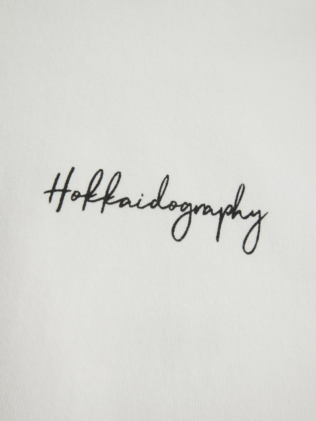 左胸に配置されたHOKKAIDOGRAPHYの筆記体ブランドロゴ。シンプルで洗練されたワンポイントデザイン。