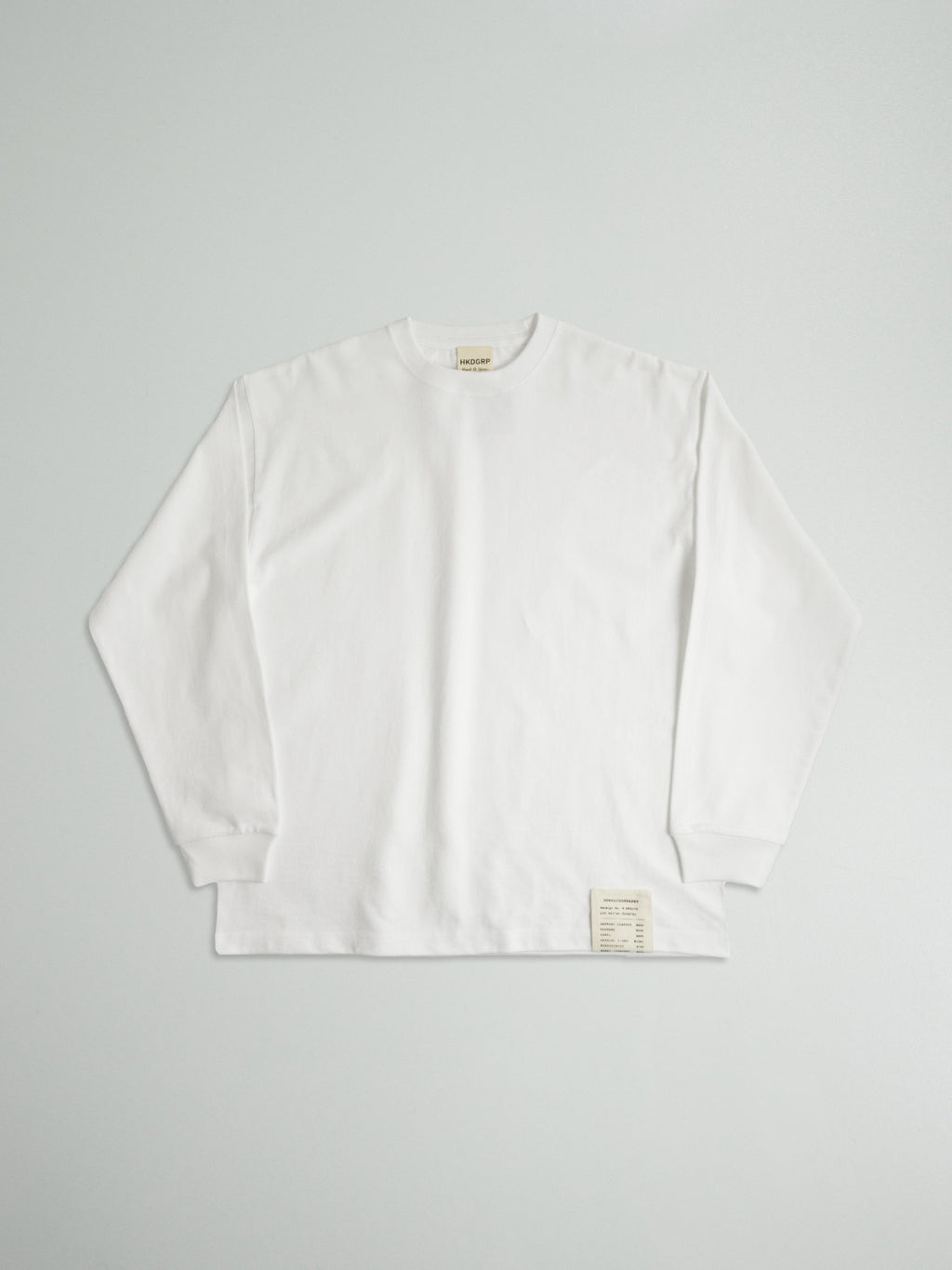 9.1oz極厚LONG SLEEVE TEE（ホワイト）の前面全体。左裾のタグが目を引くミニマルなデザイン。